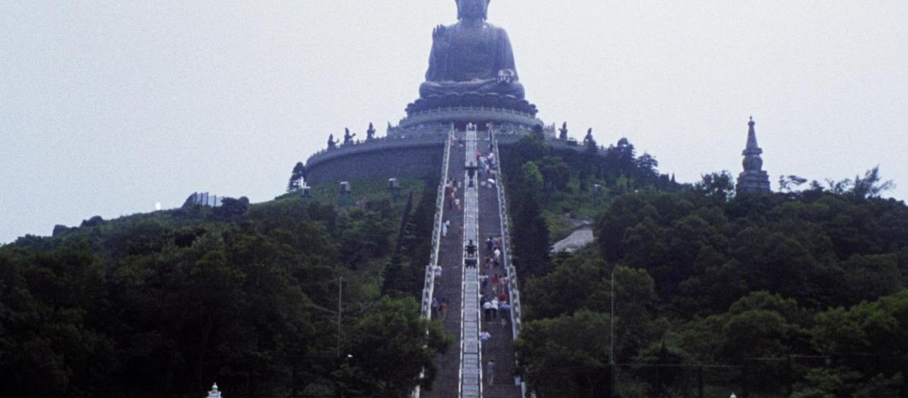 Große Buddha-Statue auf einem Hügel, mit einer langen Steintreppe und vielen Besuchern.