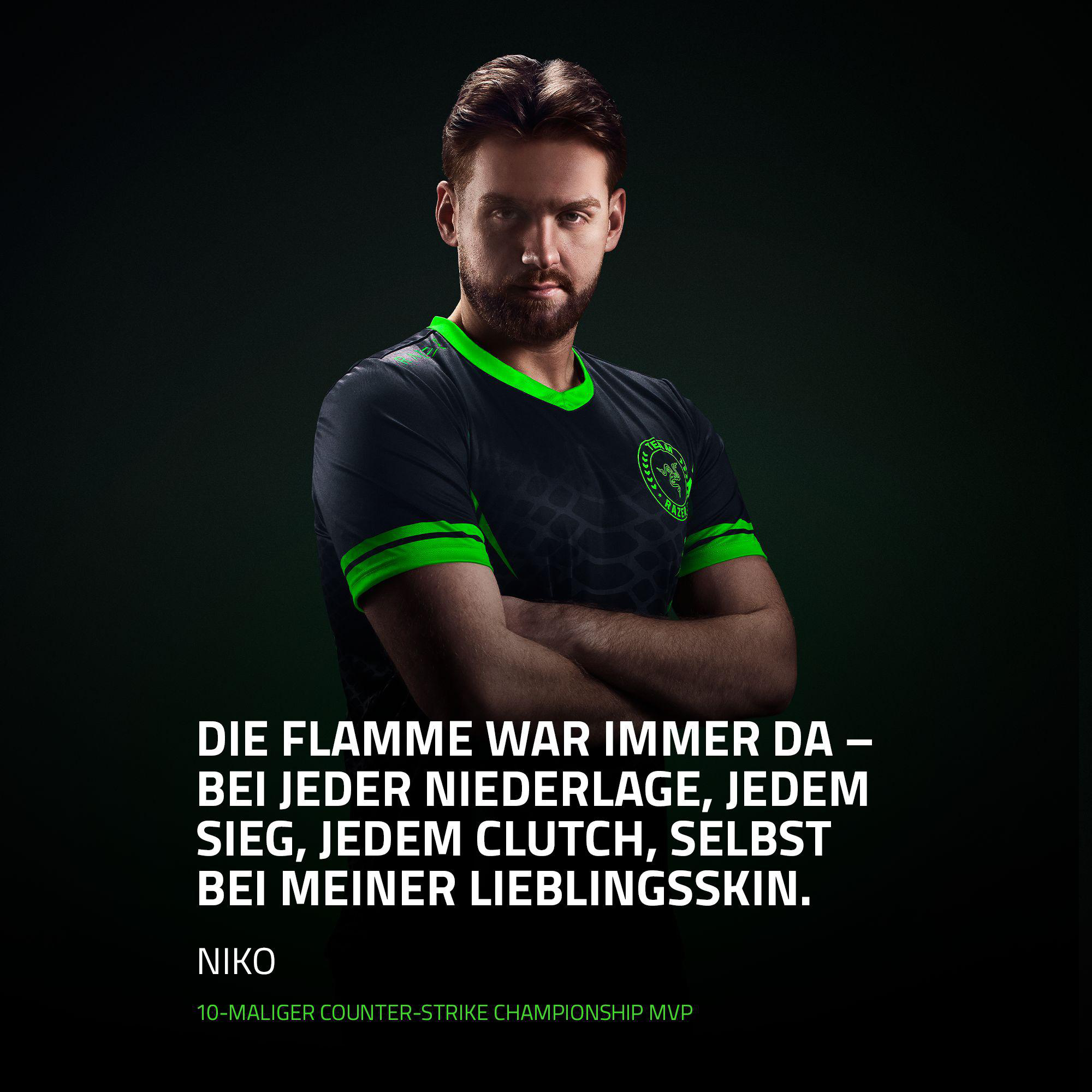Ein Mann in einem schwarzen Trikot mit grünen Streifen, der die Arme verschränkt.