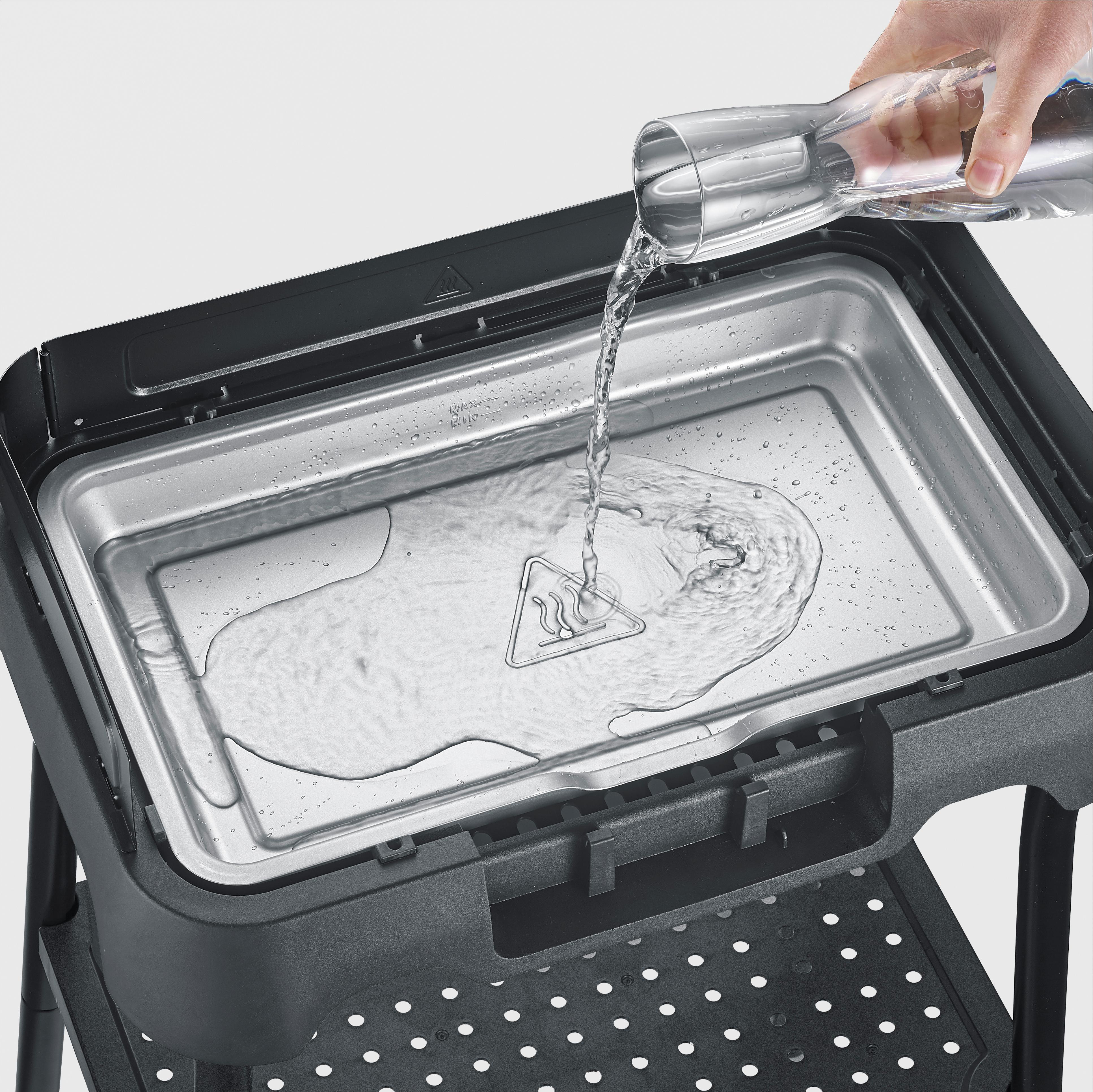 Wasser wird aus einer Karaffe in eine silberne Grillwanne gegossen.