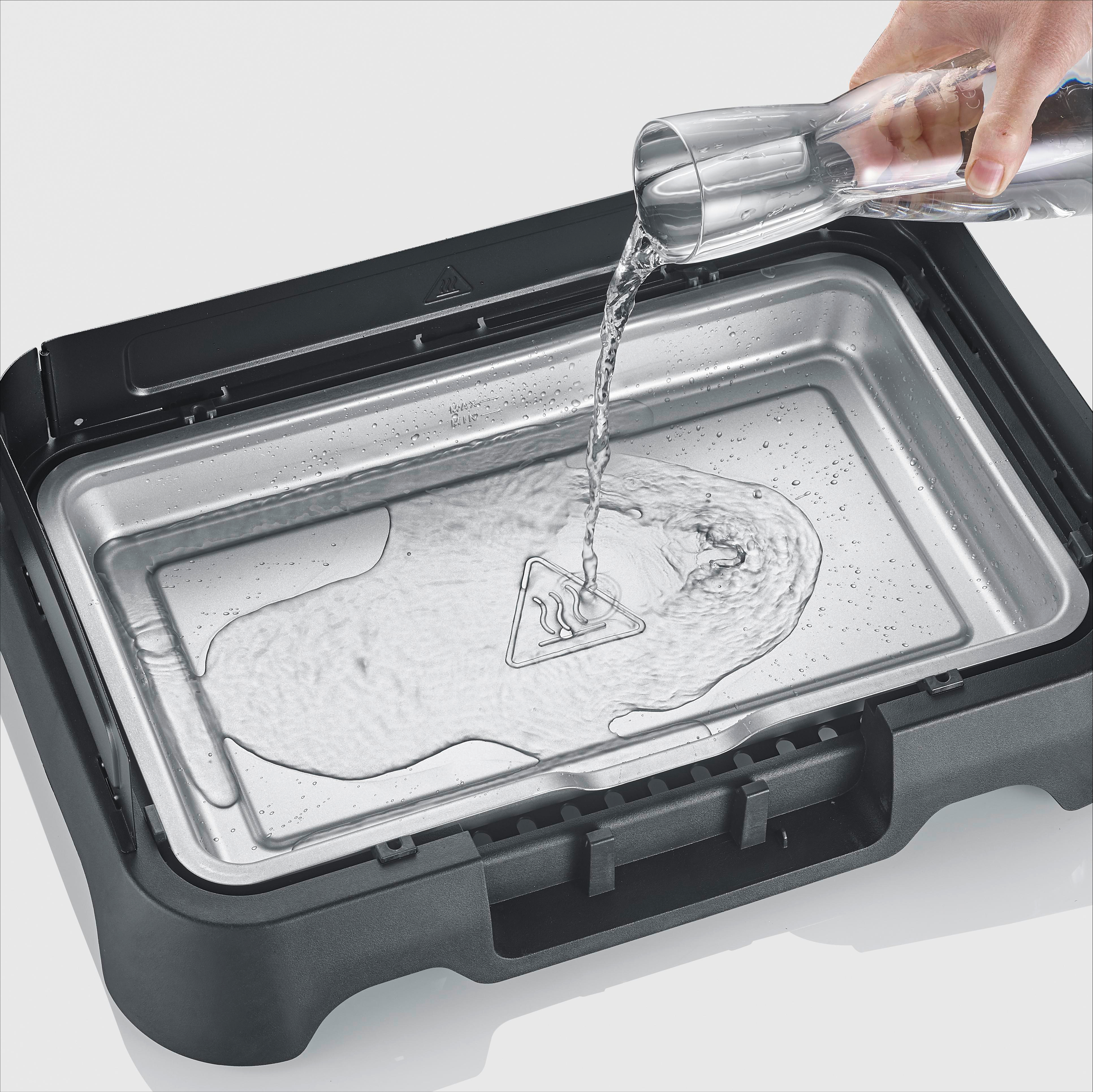 Wasser wird aus einem Glas in eine schwarze Elektrogrillpfanne gegossen.