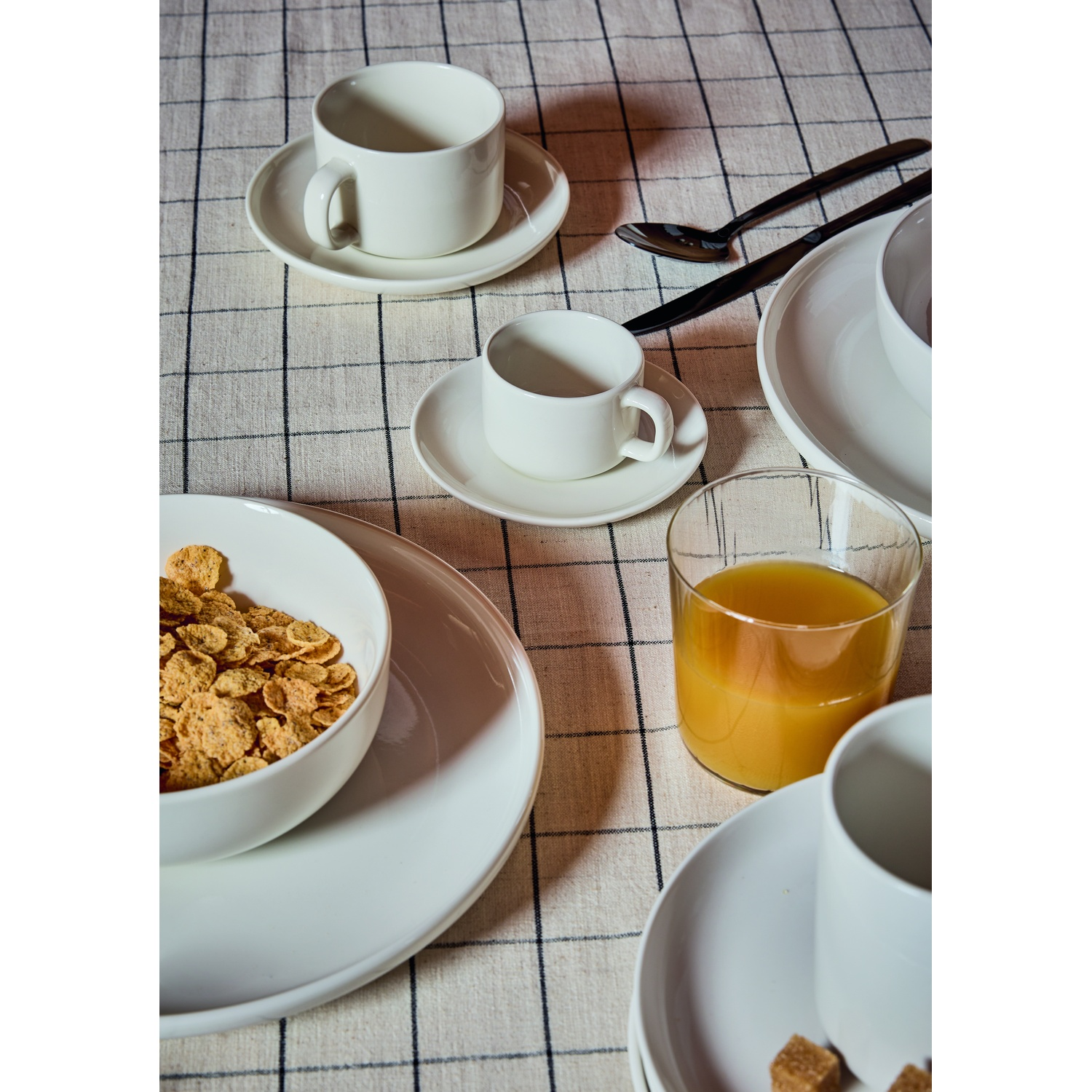 Una tavola per la colazione con cereali, succo, tazze da caffè e posate.