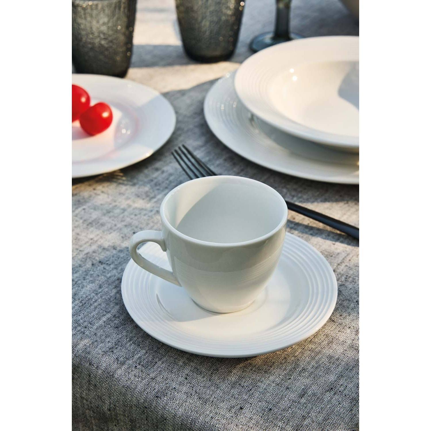 Una tazza da caffè bianca e piattino riposano su una tovaglia grigia.