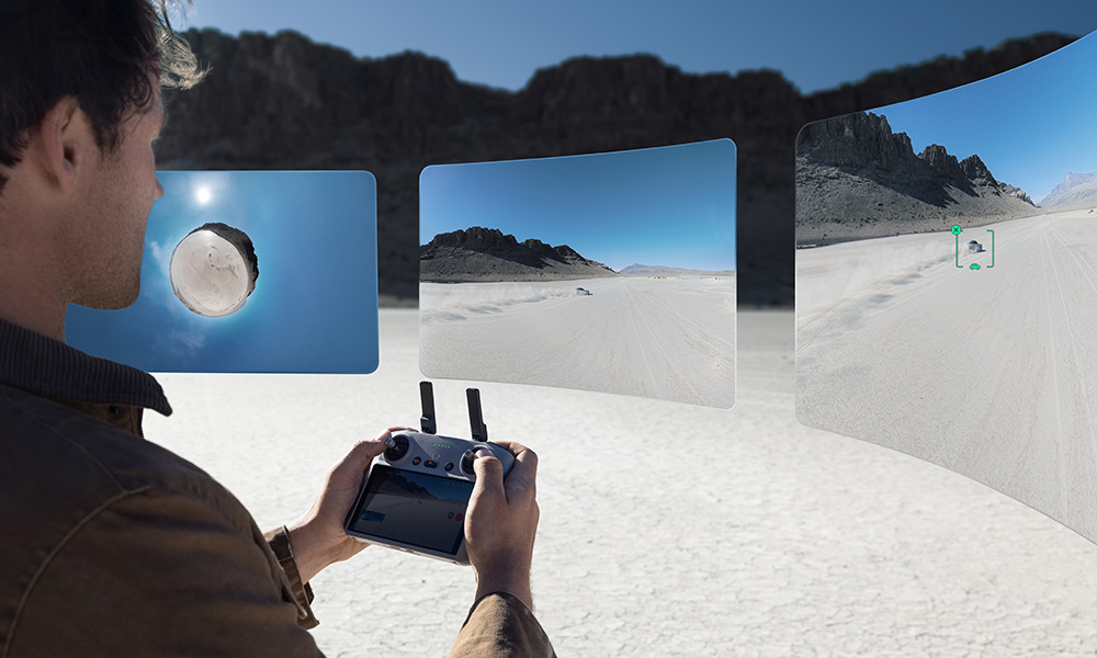 Mężczyzna steruje dronem za pomocą kontrolera na pustyni, widoczne trzy ekrany.