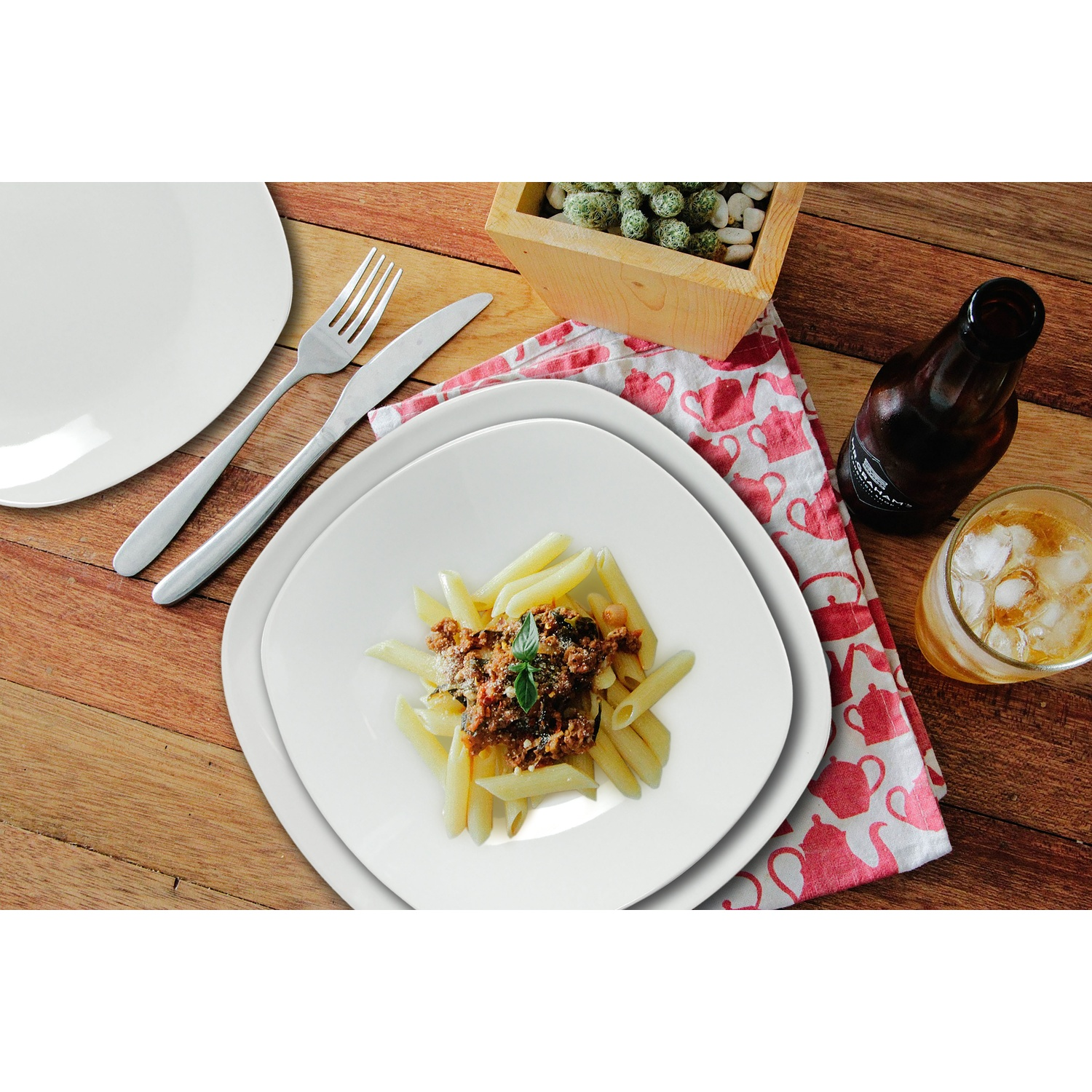 Penne con sugo su un piatto, con posate, una bevanda e un cactus vicino.