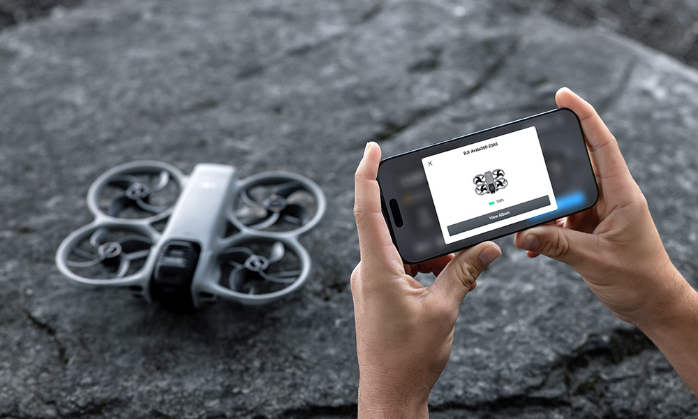 Biały dron leży na skałach, podczas gdy osoba trzyma smartfon z aplikacją drona.