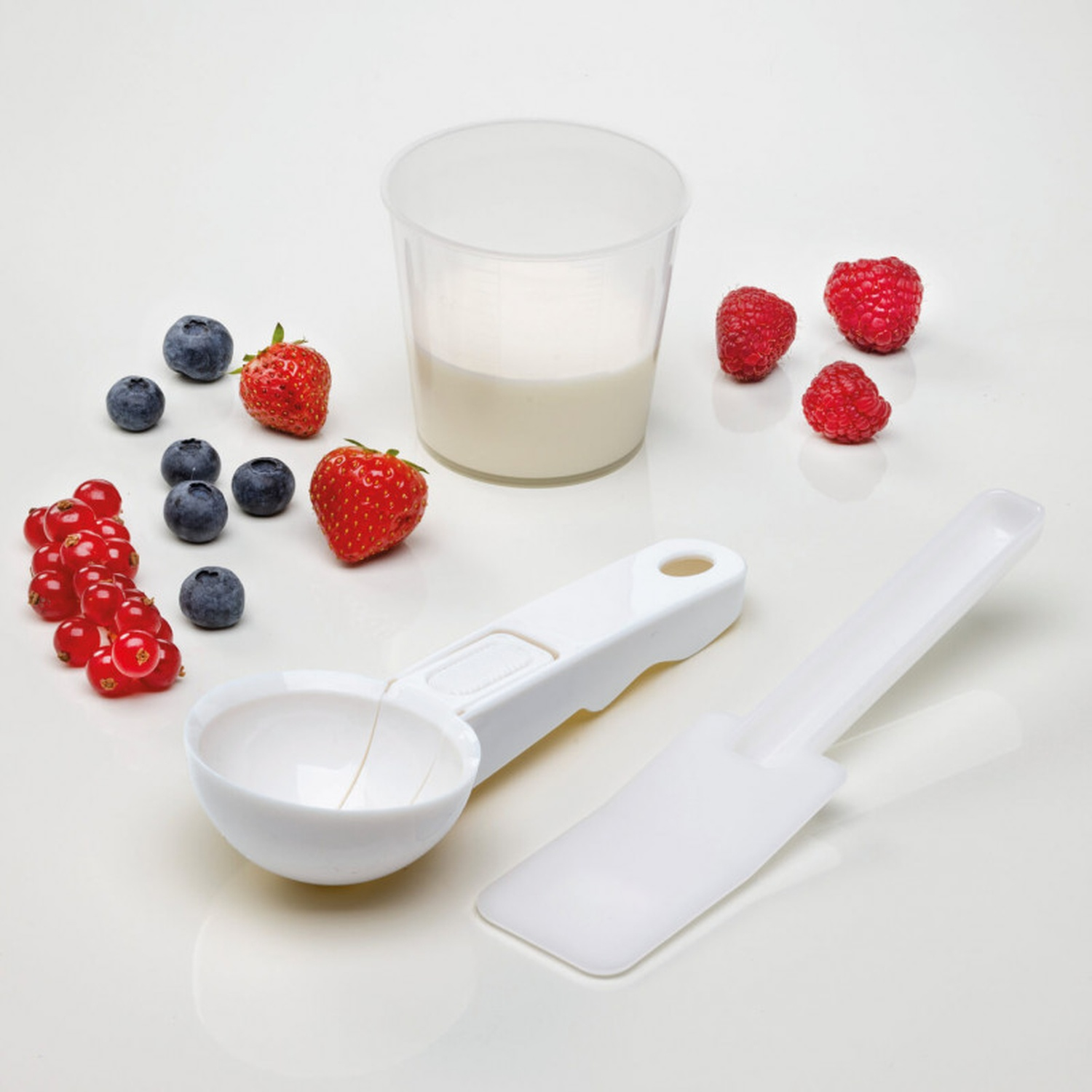 Frutti di bosco e latte con misurino e spatola su sfondo bianco.