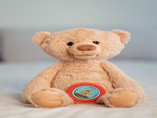 Ein beiger Teddybär sitzt auf einer gestreiften Decke und hat ein Bild auf seinem Bauch.