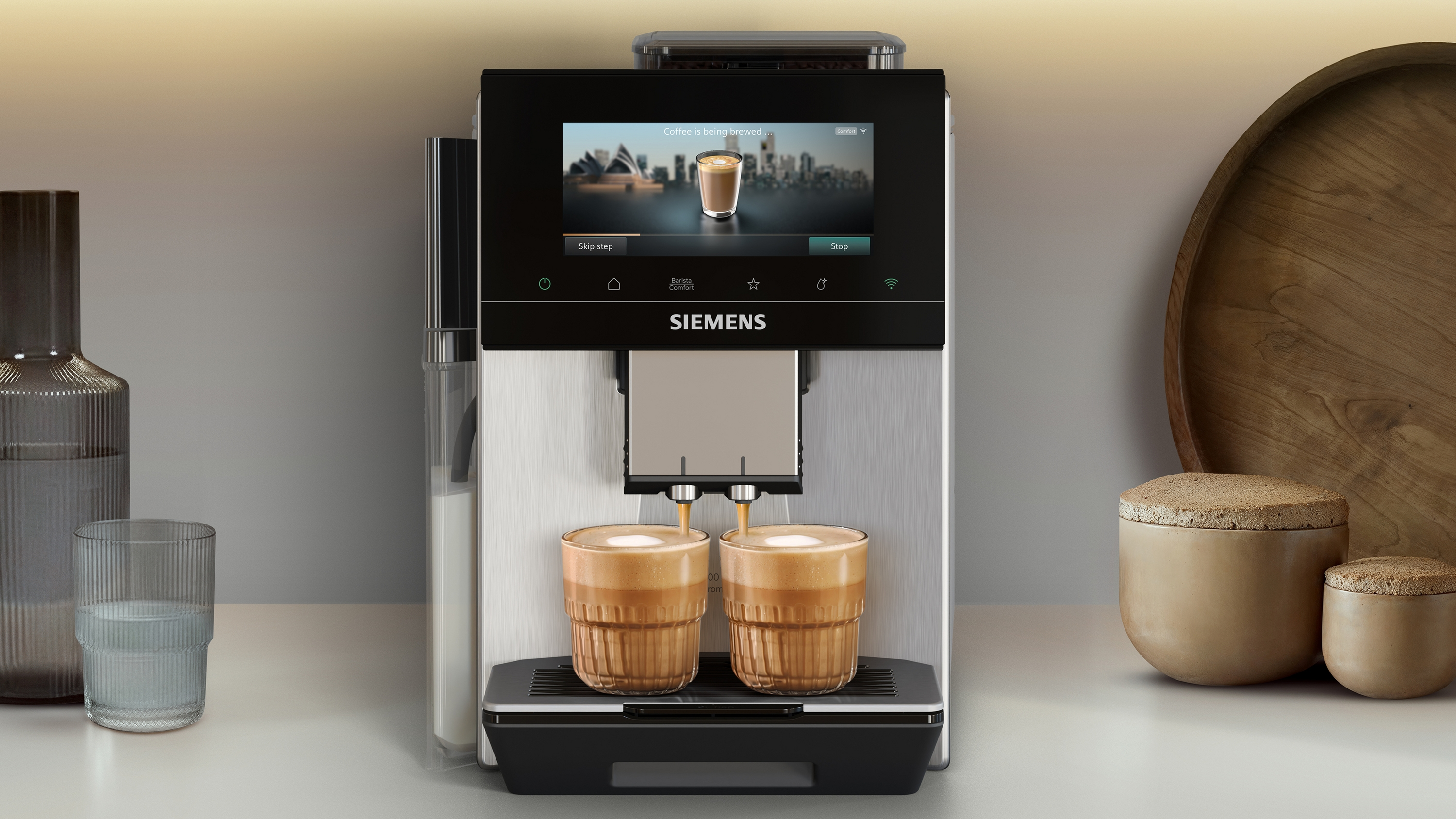 Kaffeemaschine brüht zwei Getränke in Gläser, Bildschirm zeigt Stadtansicht und Kaffee.