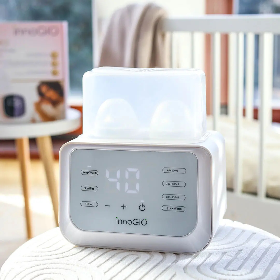 Biały podgrzewacz do butelek z cyfrowym wyświetlaczem stoi na białej tkaninie.