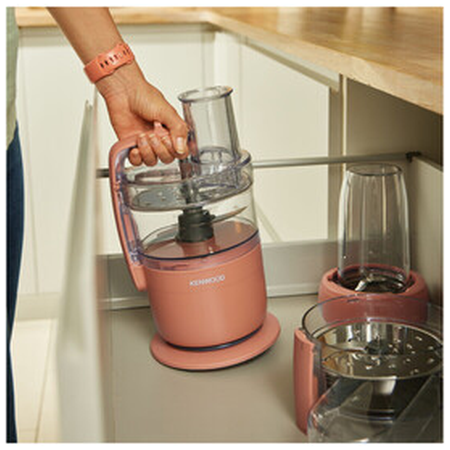 A hand reaches for a pink kitchen appliance with a clear container.