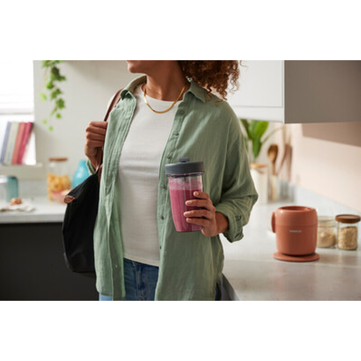 Woman holding a smoothie cup in a kitchen, with a blender and jars in background.