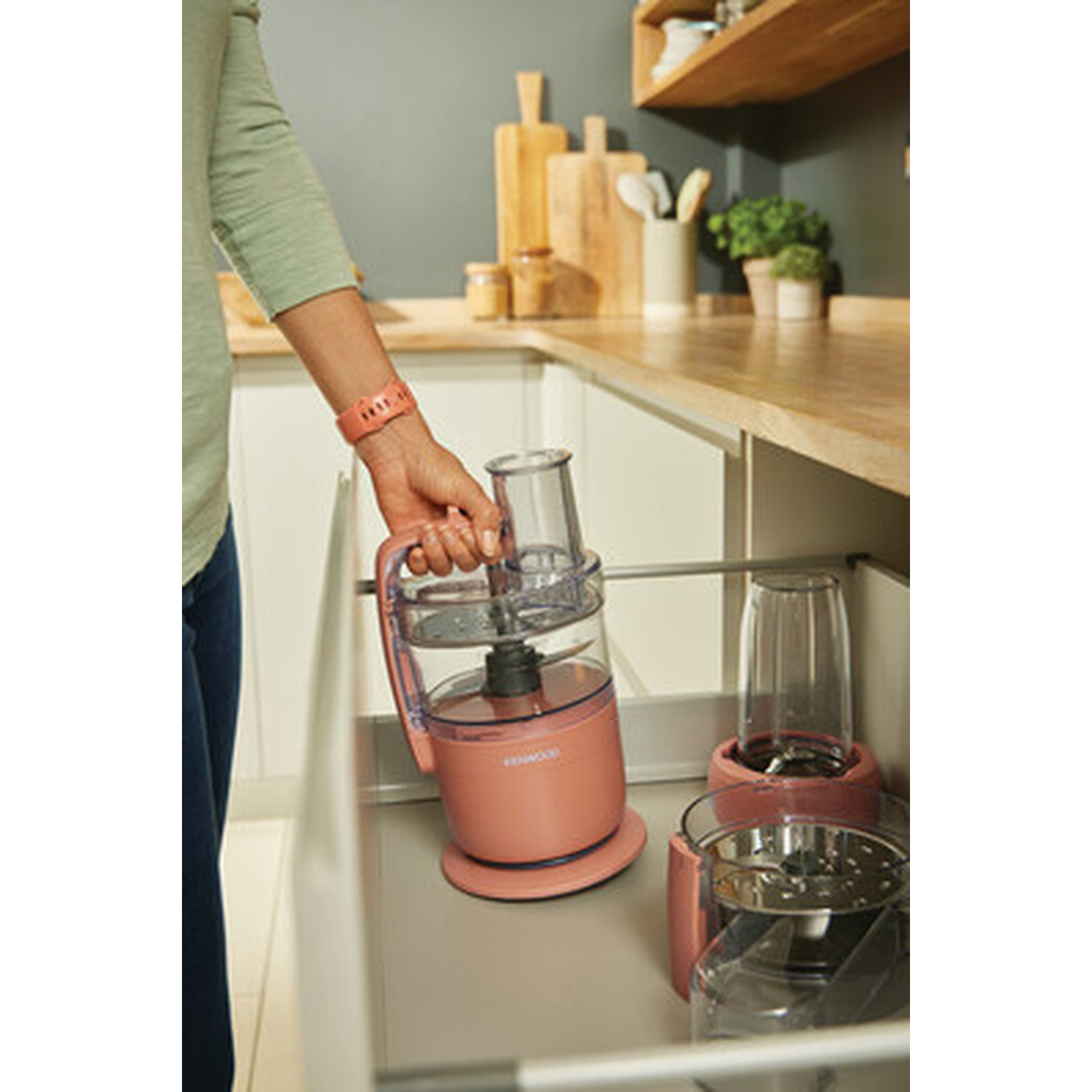 A hand picks up a pink food processor attachment from a drawer.