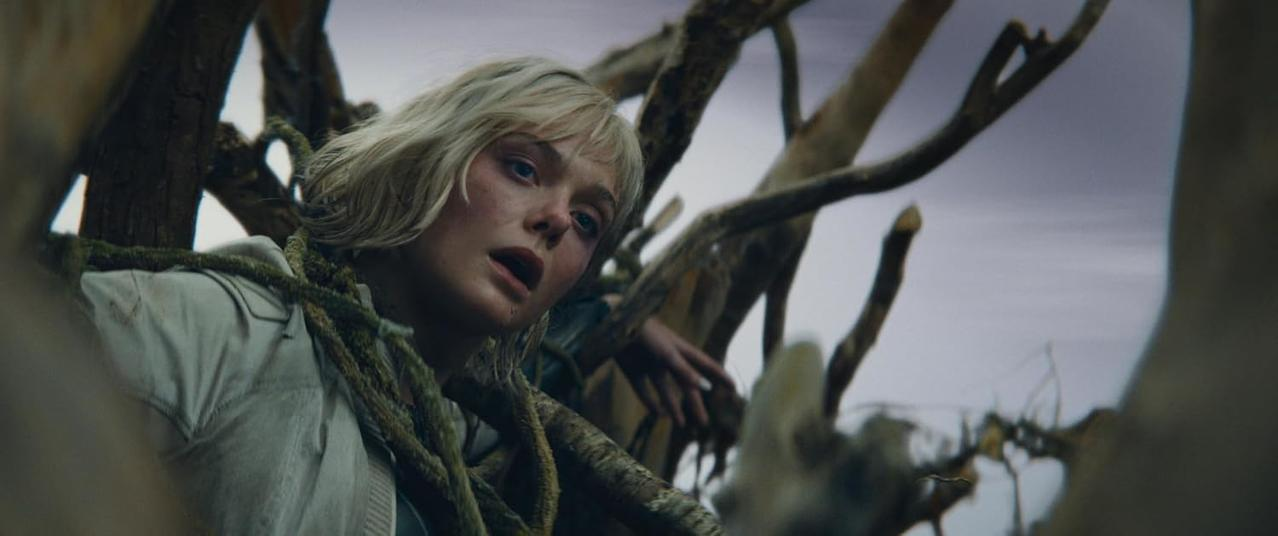 Eine blonde Frau mit Schmutz im Gesicht, gefesselt von dunklen Lianen in einem Wald.