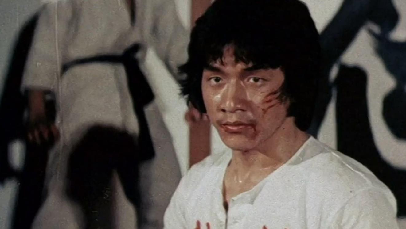 Ein asiatischer Mann mit blutigen Wunden im Gesicht trägt ein weißes T-Shirt.