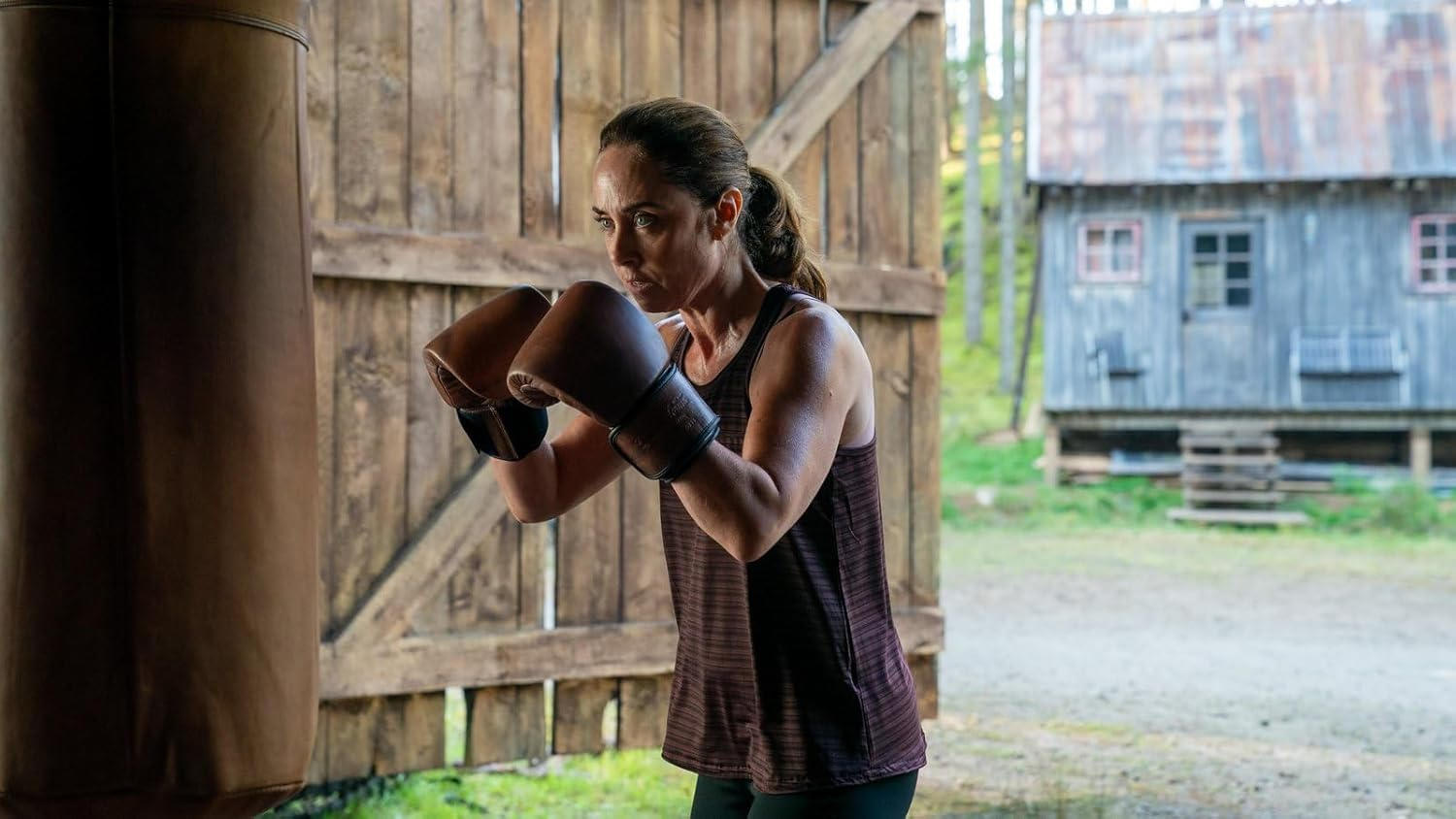 Eine Frau mit Boxhandschuhen trainiert vor einer Holzhütte.