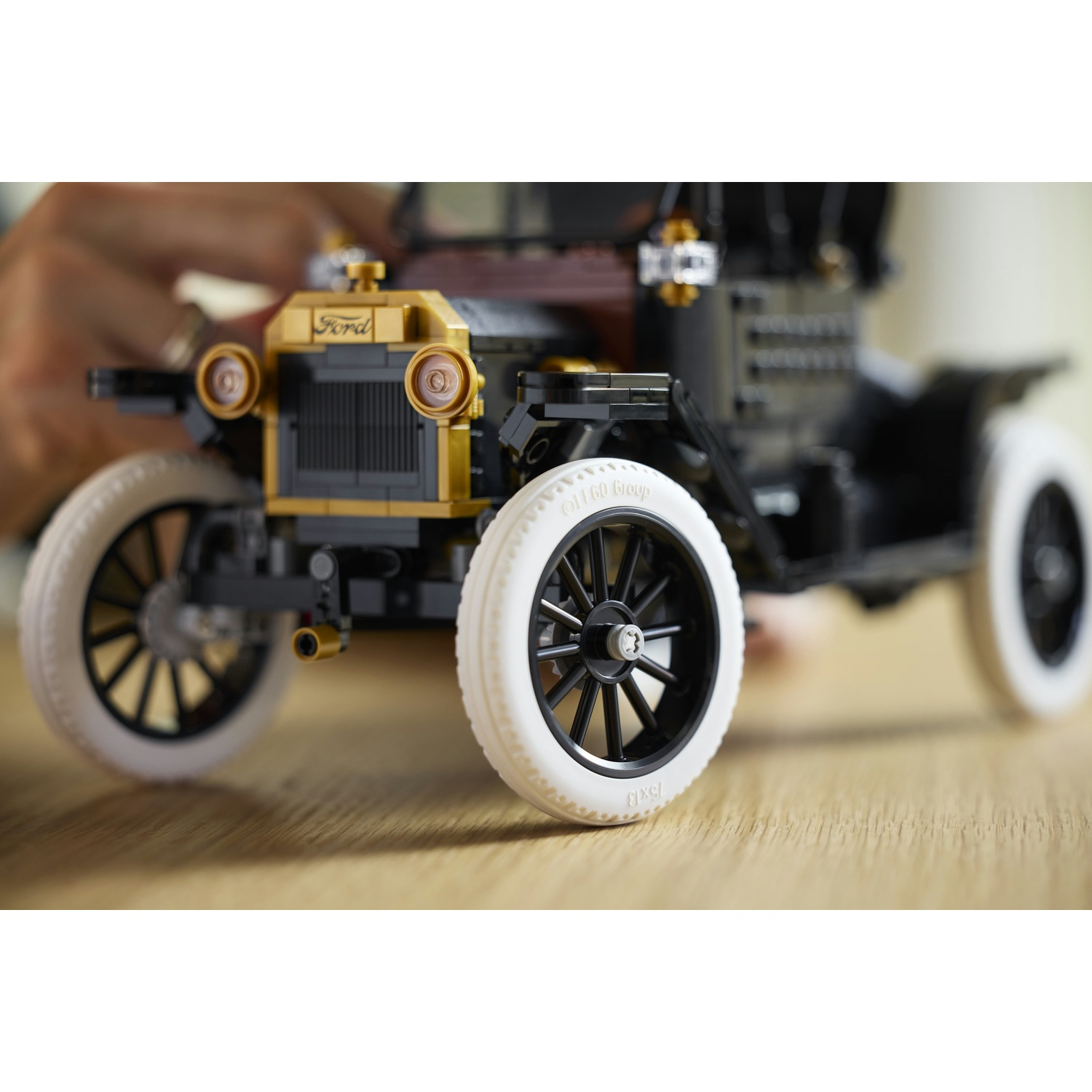 Un'auto Lego nera con griglia dorata e pneumatici bianchi siede su un tavolo di legno.