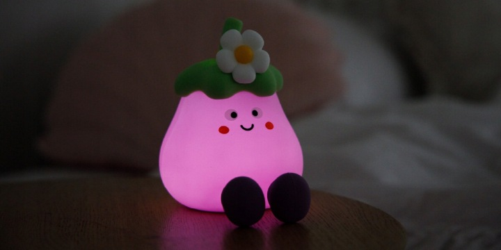 Fioletowa lampka bakłażan z twarzą i kwiatkiem siedzi na stole.