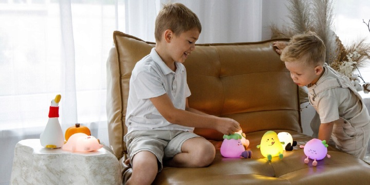 Dwóch chłopców bawi się kolorowymi lampkami owocowymi na skórzanej kanapie.