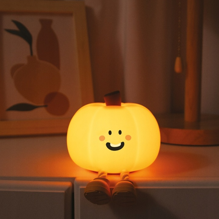 Świecąca lampa dyniowa z uroczą twarzą siedzi na półce.