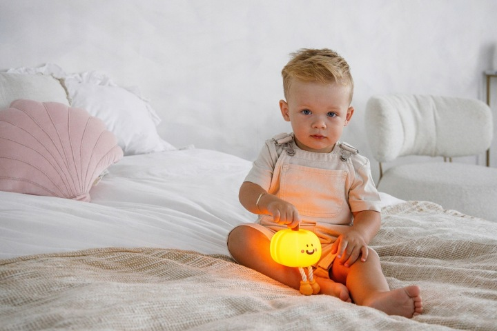 Mały chłopiec siedzi na łóżku, trzymając świecącą latarkę w kształcie dyni.