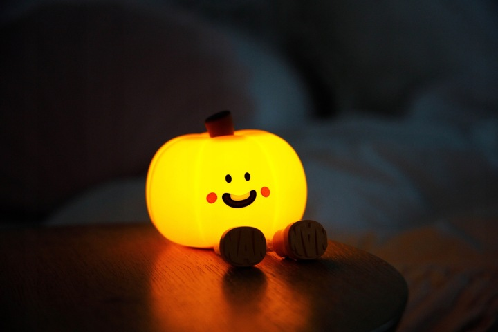 Świecąca lampka dynia z twarzą siedzi na drewnianym stole.