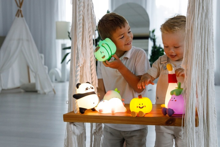 Dwóch chłopców na huśtawce makramowej z uroczymi nocnymi lampkami w kształcie zwierząt i warzyw.