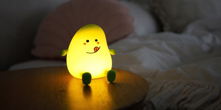 Świecąca lampka awokado stoi na stoliku nocnym. Ma uroczą buźkę.