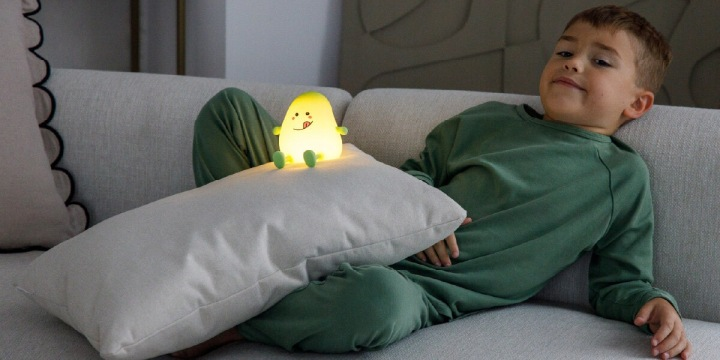 Chłopiec siedzi na kanapie obok świecącej lampki w kształcie owocu.