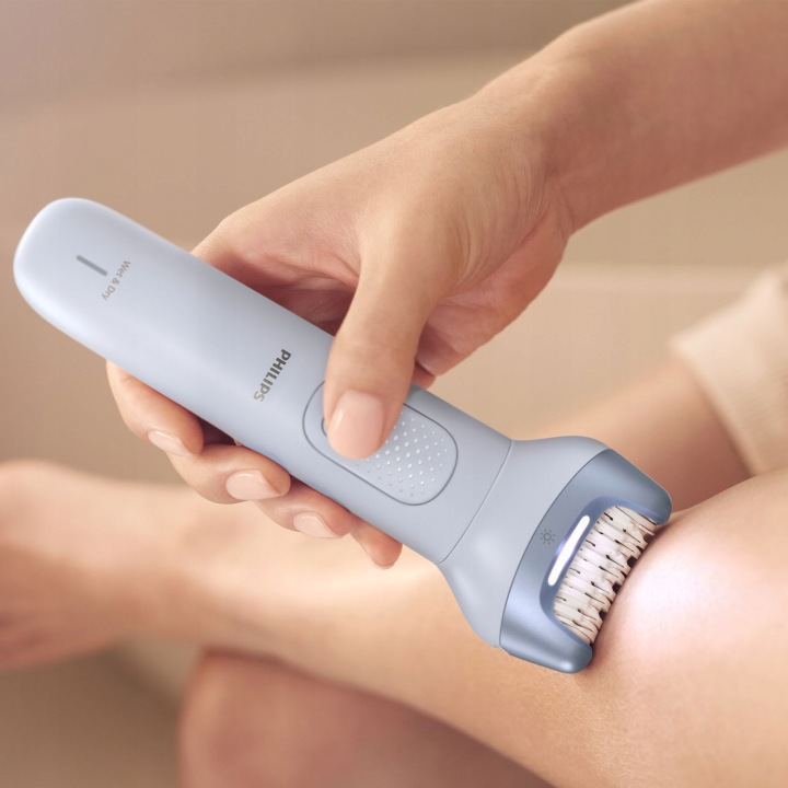 Osoba używa jasnoniebieskiej depilarki Philips na nodze.