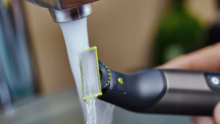 Osoba płucze ciemnoszarą elektryczną maszynkę z żółtymi akcentami pod bieżącą wodą.