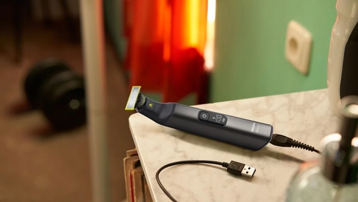 Ciemny trymer z żółtą krawędzią spoczywa na marmurowej powierzchni, podłączony do kabla USB.