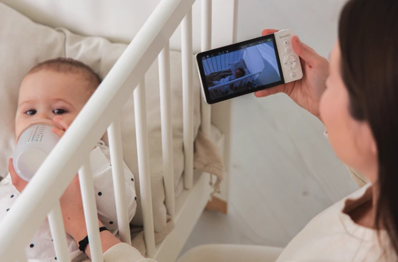 Matka patrzy na nianię elektroniczną, gdy dziecko pije w łóżeczku.