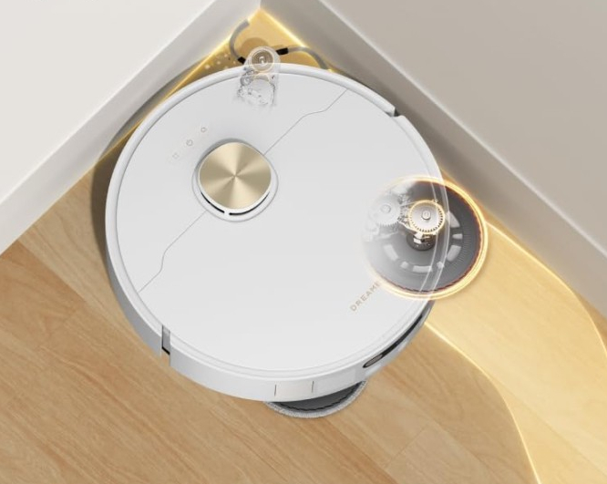 Biały robot sprzątający ze złotym przyciskiem czyści drewnianą podłogę.