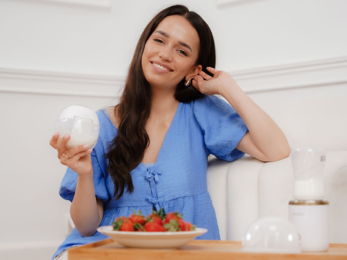 Kobieta w niebieskiej sukience trzyma pojemnik, truskawki na talerzu, białe tło.
