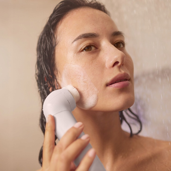 Kobieta myje twarz elektryczną szczoteczką do mycia pod prysznicem.