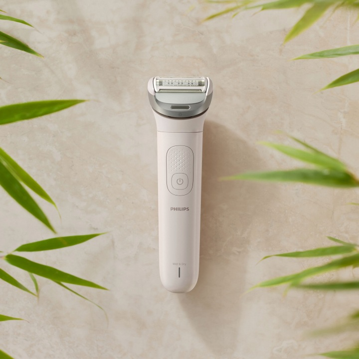 Biały trymer Philips z ostrzem, otoczony zielonymi liśćmi bambusa.