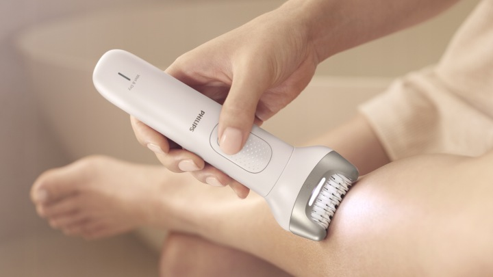 Dłoń trzyma białą depilarkę Philips używaną na nodze.