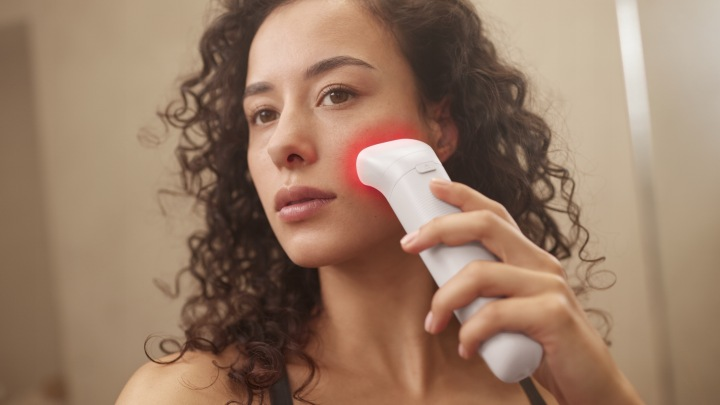 Kobieta z ciemnymi kręconymi włosami używa białego urządzenia do pielęgnacji skóry.