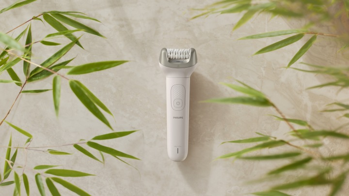 Biały depilator Philips na beżowym tle, otoczony zielonymi liśćmi bambusa.