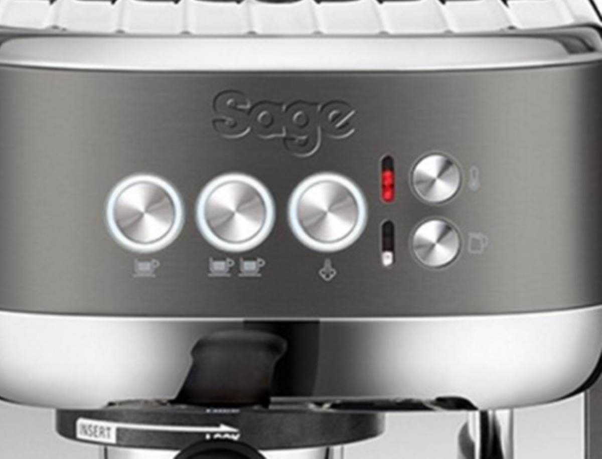 Zbliżenie srebrnej ekspresu do kawy z podświetlanymi przyciskami i logo 'Sage'.
