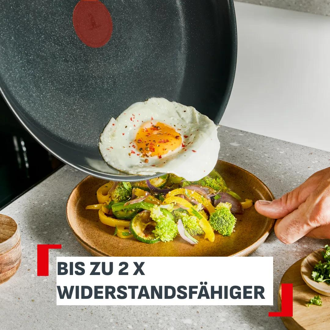 Ein Spiegelei wird über sautiertes Gemüse in einer Pfanne auf einen Teller gegeben.