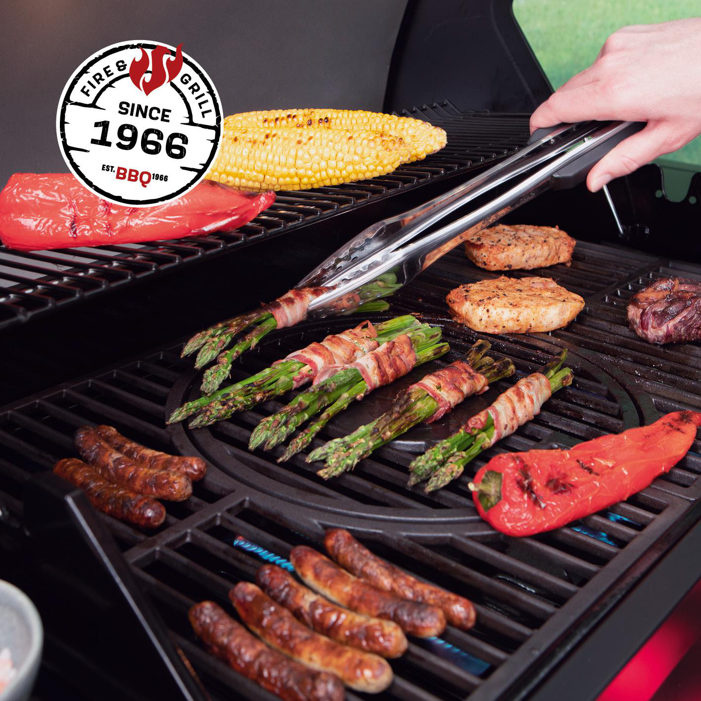 Speckumwickelter Spargel, Würstchen, Mais und Paprika auf einem Grill.