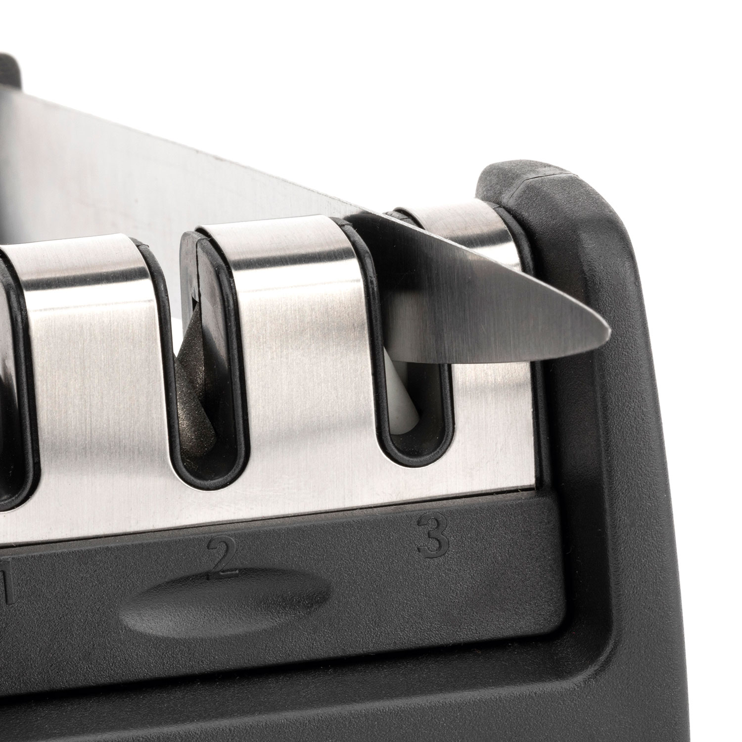 Un cuchillo de cocina se afila en un afilador de cuchillos negro y plateado de tres ranuras.