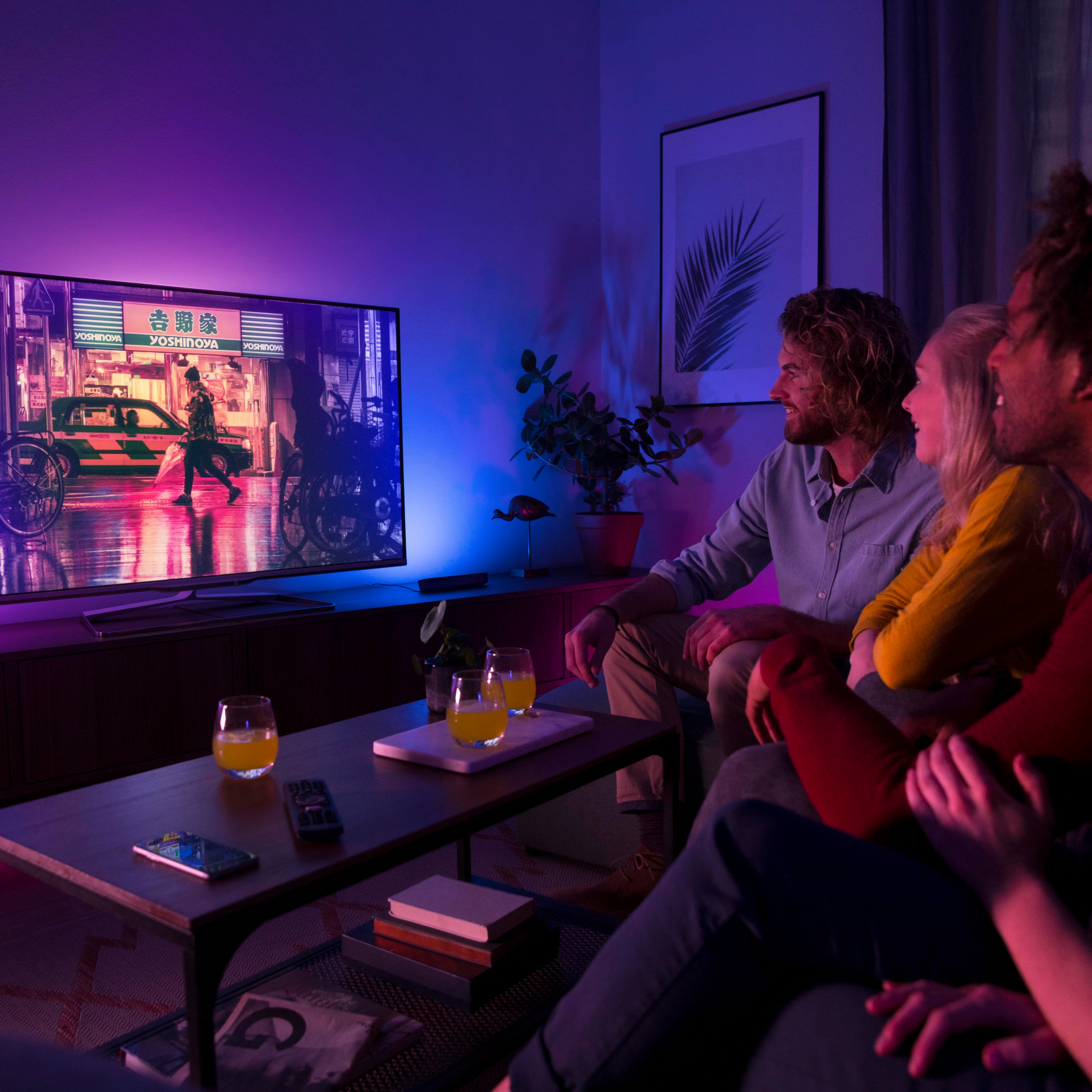 Vier Freunde schauen fern, beleuchtet von lila Licht. Ein japanisches Restaurant ist auf dem Fernseher.