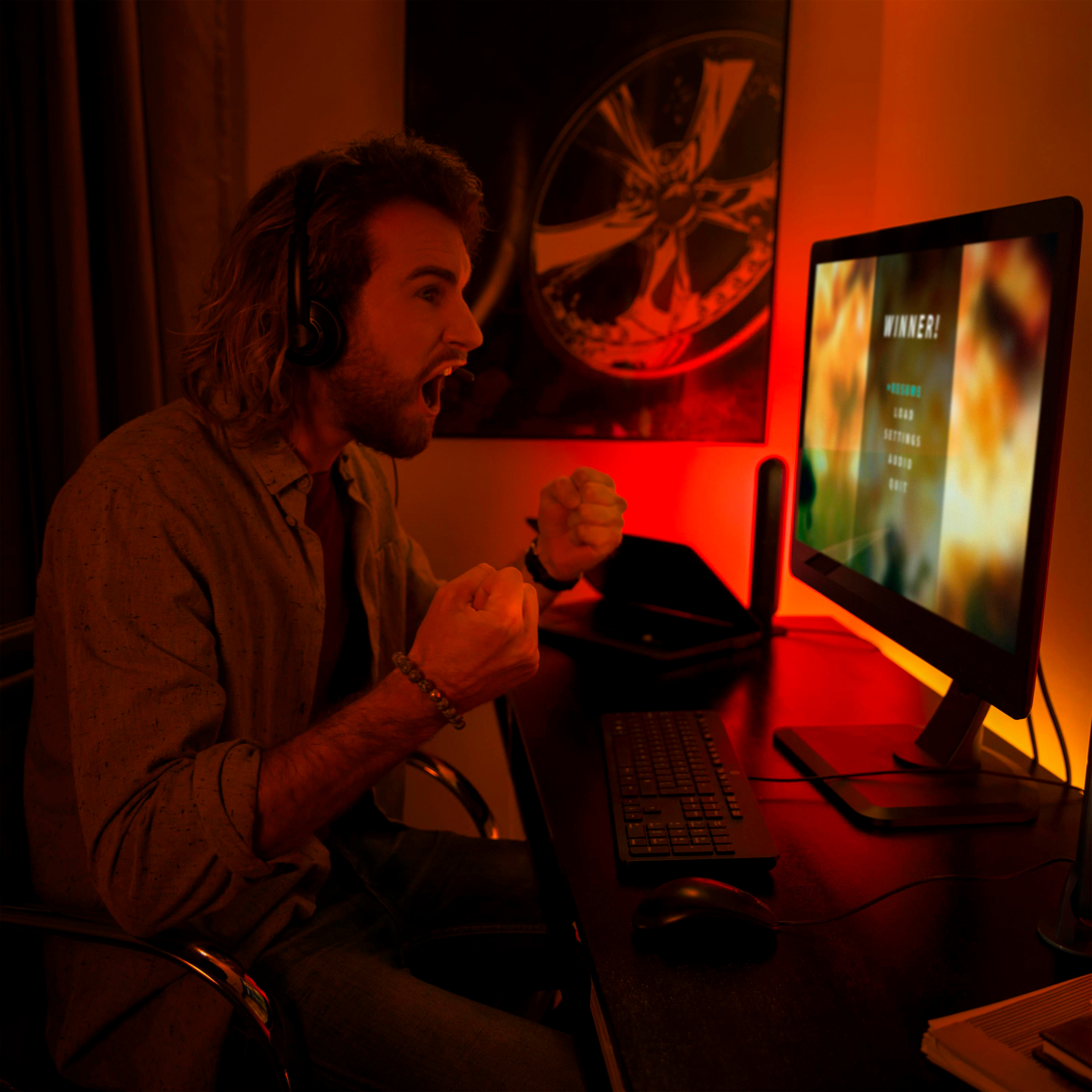 Mann mit Kopfhörern jubelt vor einem Computermonitor mit 