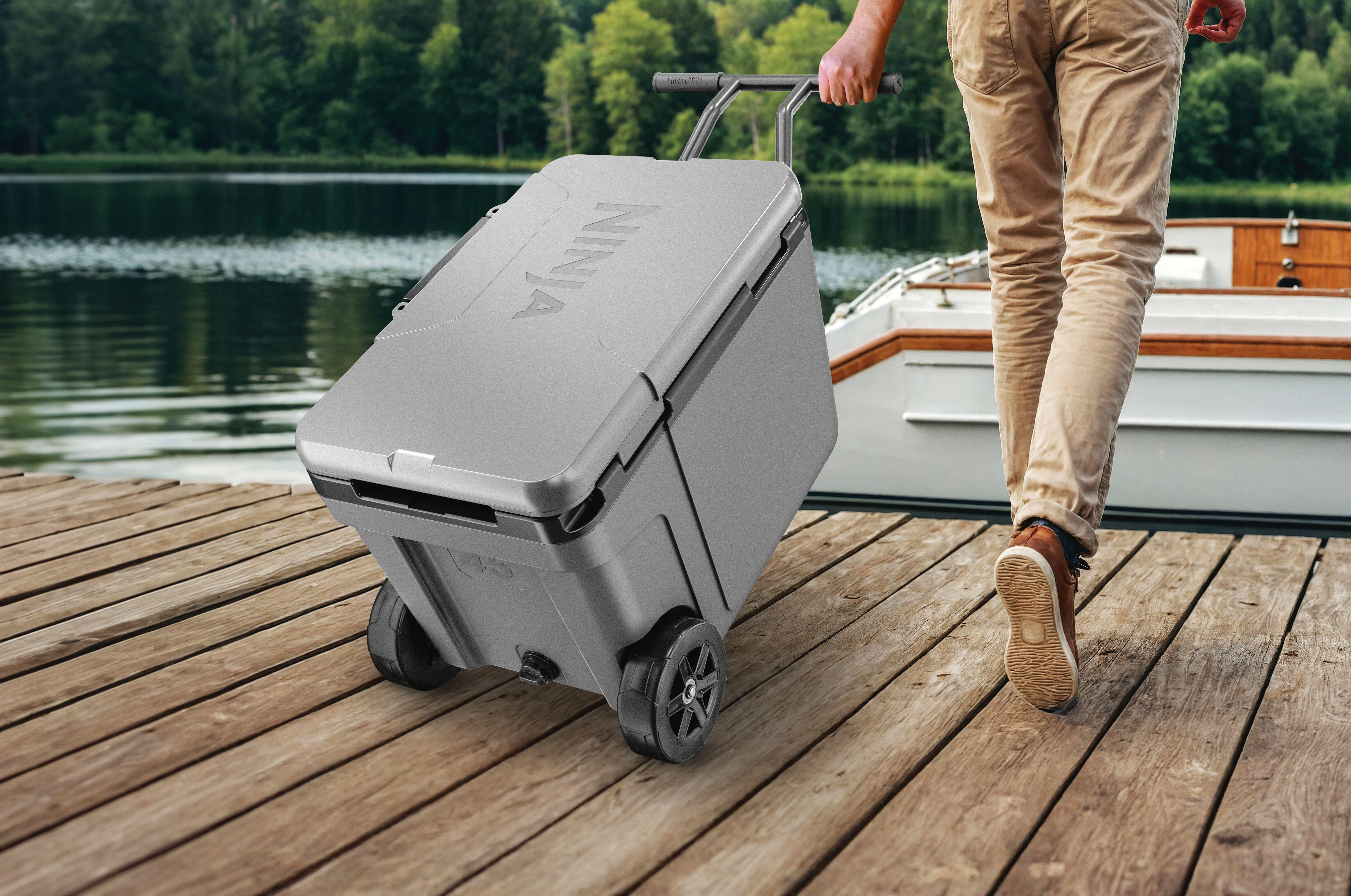 Grauer Kühlbox mit Rädern auf Holzsteg, Mann zieht ihn zum Boot.