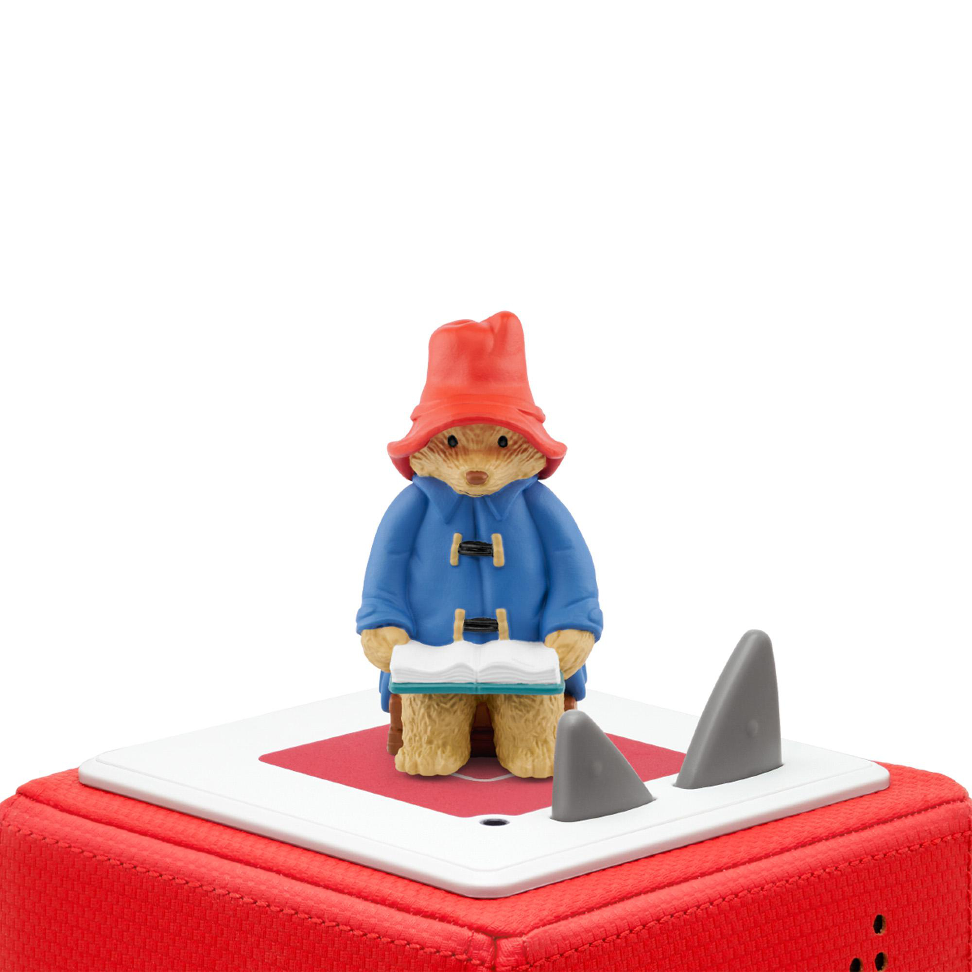 Paddington Bär mit Buch steht auf Spielzeug, Haifischflossen ragen heraus.