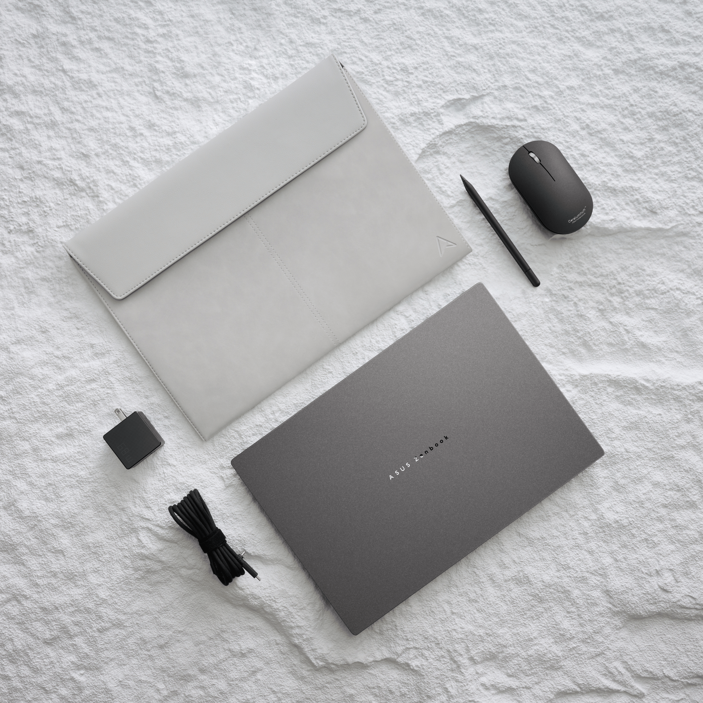 Grauer Laptop, Hülle, Stift, Maus und Ladegerät auf weißer strukturierter Oberfläche.