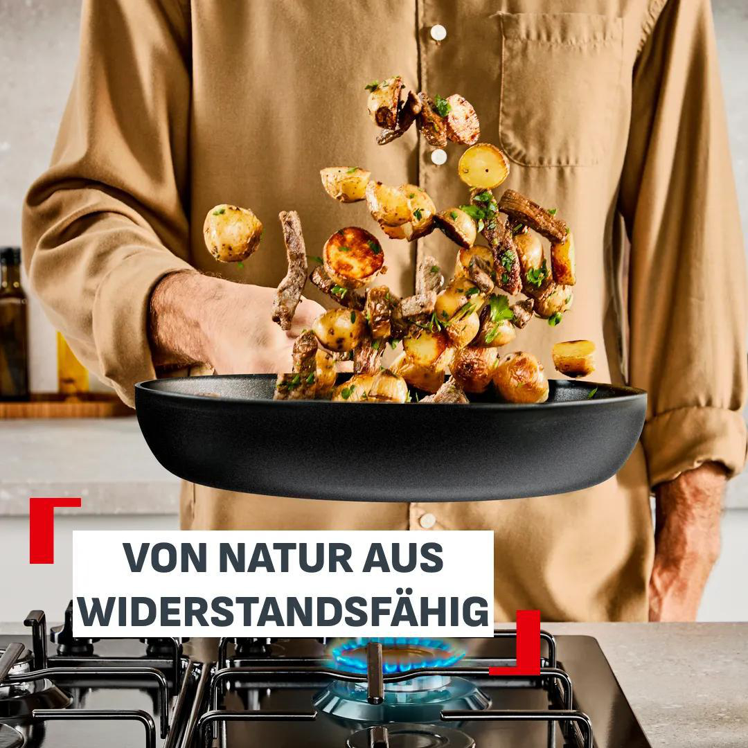 Eine Person wirft Essen in einer Pfanne über einem Gasherd. Text: 'VON NATUR AUS WIDERSTANDSFÄHIG'.