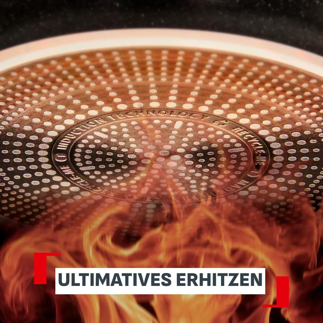 Nahaufnahme eines runden, kupferfarbenen Pfannenbodens mit Punktmuster, umgeben von orangefarbenen Flammen.